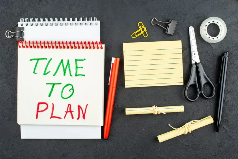 Notebook with "Time to Plan" text sits alongside red pens, paper clips, and a binder clip. Blank index cards, scissors, tape, and rolled notes complete this essential toolkit for drafting a Storm Response Plan for Commercial Properties on a dark surface.